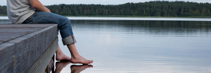 Man sitting in a deck with his foots by the water of a big lake.