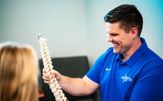 Dr. Curtis Legg showing a plastic copy of the spine to a patient during a chiropractic consultation.
